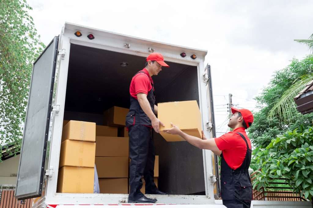 Millsboro movers in red shirts and black overalls loading boxes into the back of a truck 
