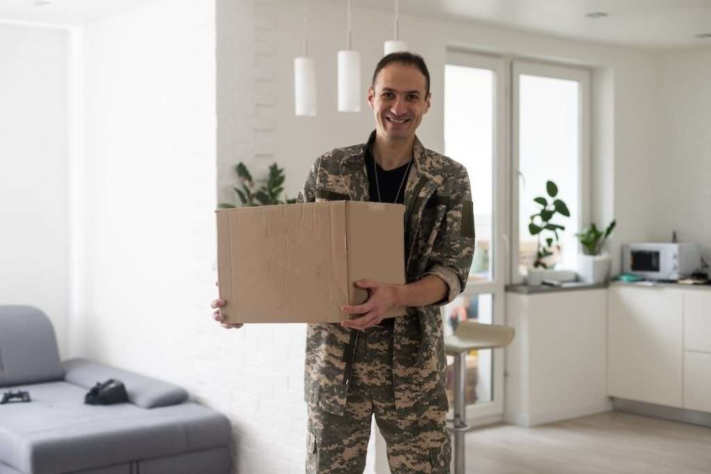 A smiling soldier wearing camouflage holding a box and getting ready to move