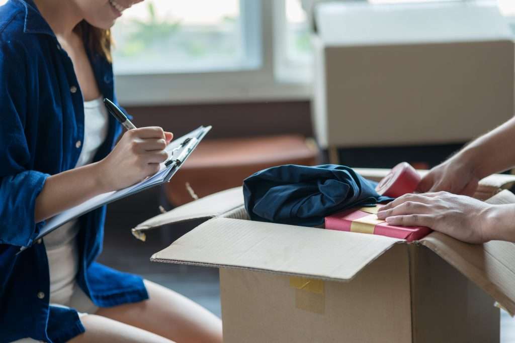 A person packing a box while another fills out info on a clipboard.